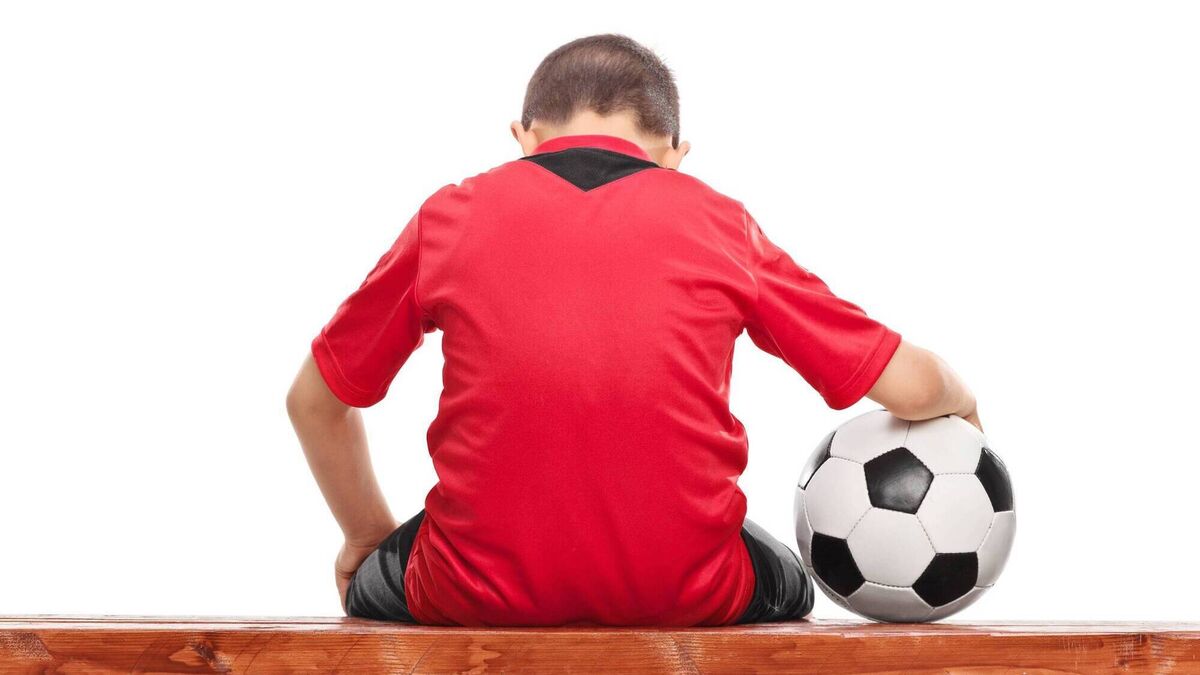Sad little boy in red soccer jersey seated on bench